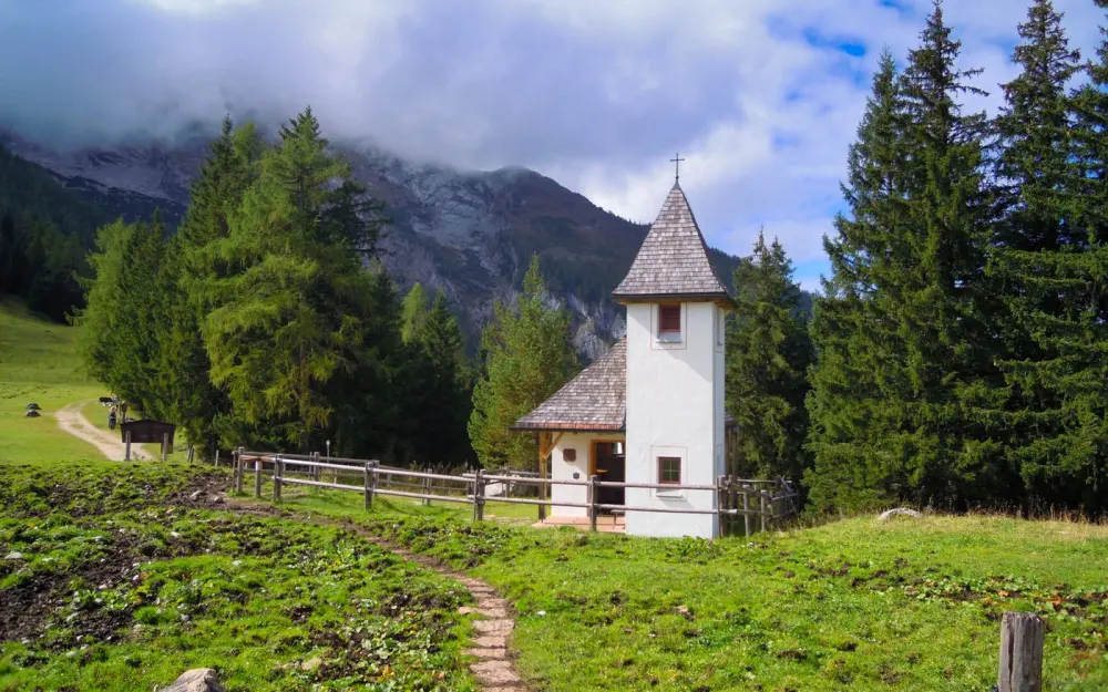 Symbolbild: A quaint chapel set against the picturesque Bavarian mountains with lush greenery and a clear sky.