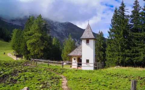 Symbolbild: A quaint chapel set against the picturesque Bavarian mountains with lush greenery and a clear sky.