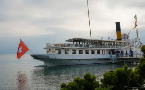 Symbolbild: A scenic view of a classic boat docked at a peaceful Swiss port with flags waving.