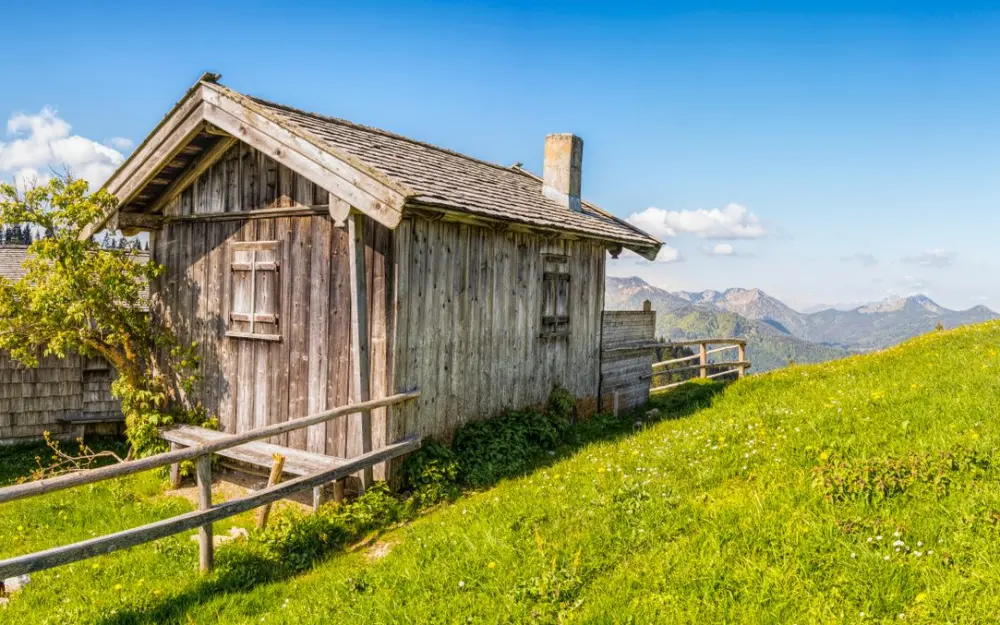 Symbolbild: Charming wooden cabin set in a lush meadow with picturesque mountain views.