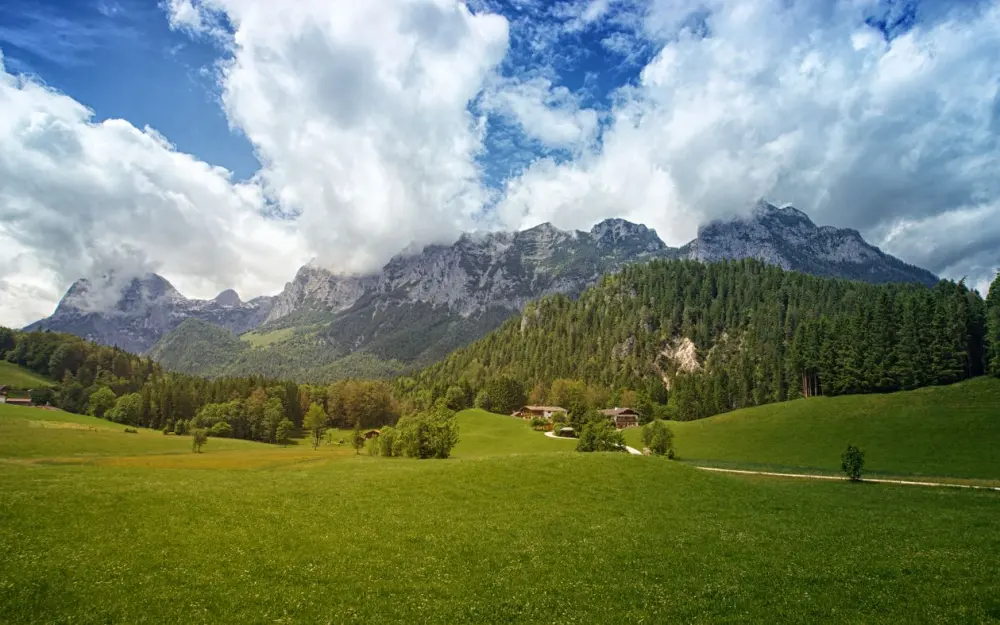 Symbolbild: Breathtaking alpine scenery featuring lush green fields, towering mountains, and fluffy clouds.