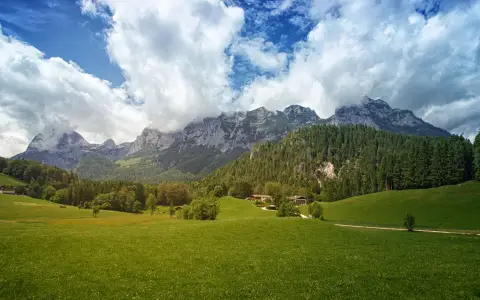 Symbolbild: Breathtaking alpine scenery featuring lush green fields, towering mountains, and fluffy clouds.