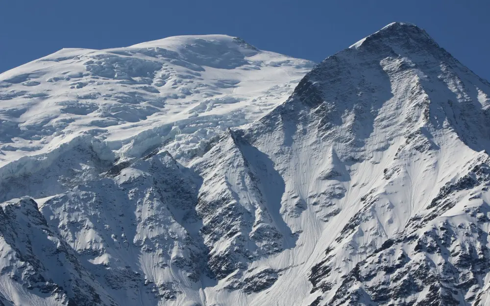 Symbolbild: A breathtaking view of snow-covered mountain peaks under a clear blue sky, capturing winter's splendor.