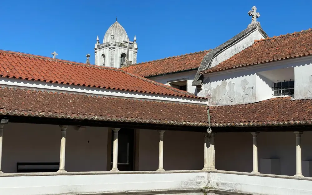 Symbolbild: A serene view of a historical monastery with a courtyard in Aveiro, Portugal under a clear blue sky.