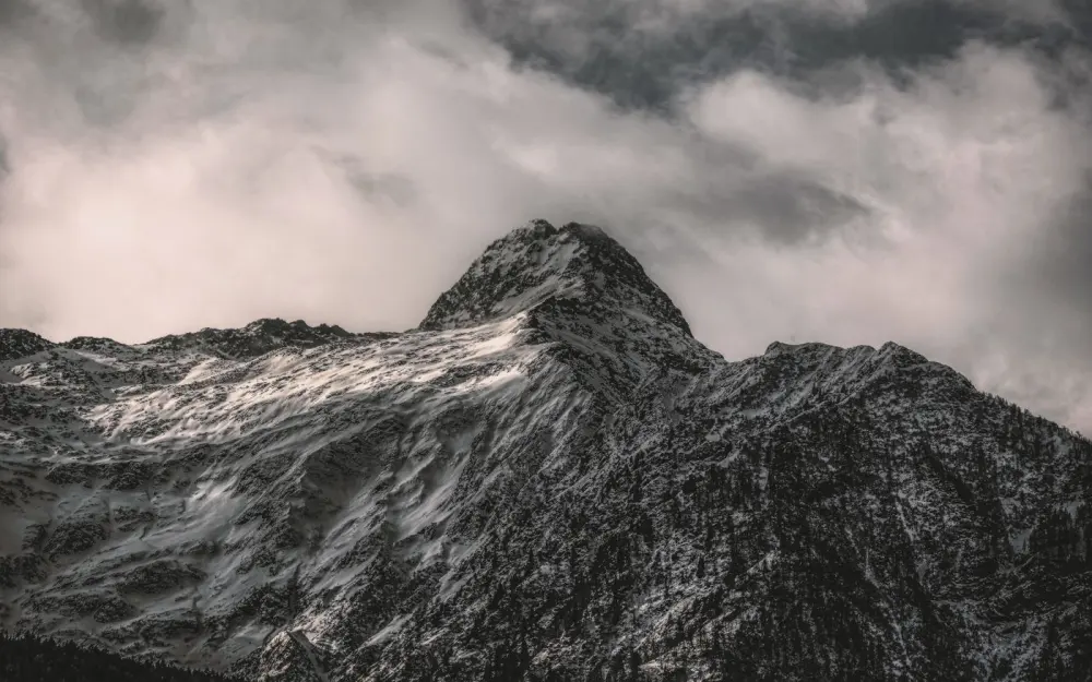 Symbolbild: A breathtaking view of a snow-covered mountain peak under dramatic clouds in Rossura, Switzerland.