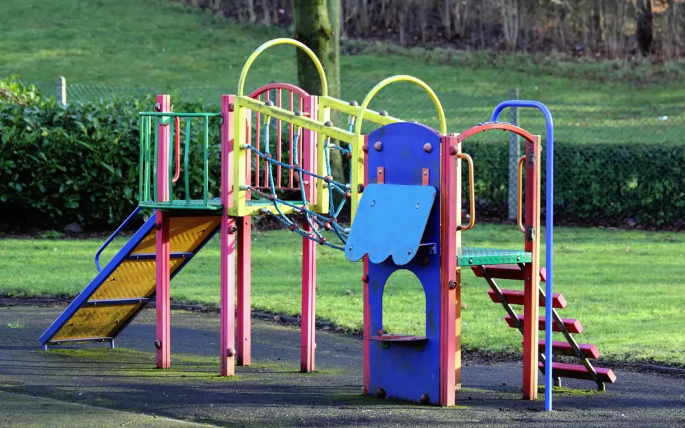 Symbolbild: Vibrant playground equipment in an open park surrounded by grass and trees.