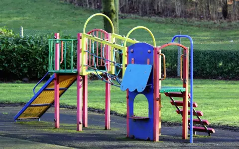 Symbolbild: Vibrant playground equipment in an open park surrounded by grass and trees.