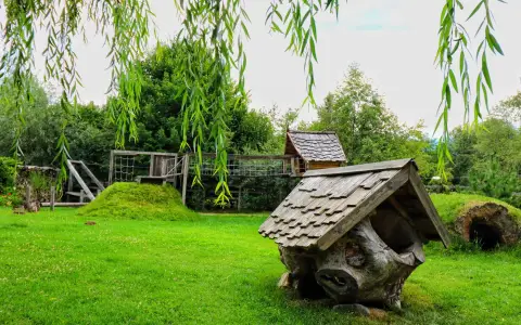Symbolbild: Charming rustic playground with wooden structures surrounded by lush greenery.
