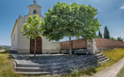 Symbolbild: A serene chapel surrounded by trees and countryside under a blue sky.