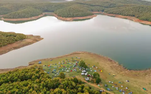 Symbolbild: Aerial view of colorful tents by a tranquil lake surrounded by lush forests.