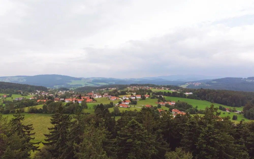 Symbolbild: Aerial view of a peaceful Bavarian village surrounded by lush greenery and rolling hills under a cloudy sky.
