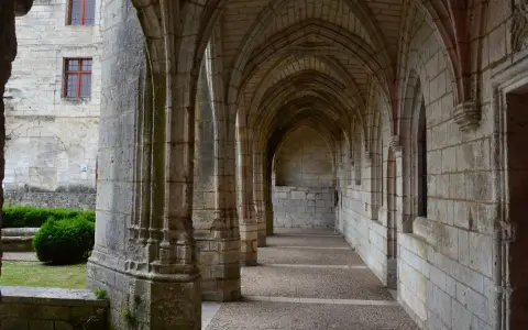 Symbolbild: A serene gothic cloister passage featuring arched stone columns and a tranquil atmosphere.