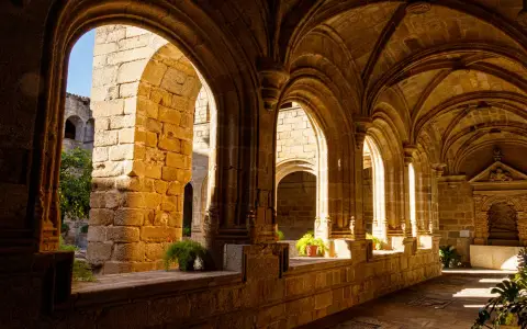 Symbolbild: Warm sunlight bathes ancient stone arches in a serene cloister passageway, evoking history and tranquility.