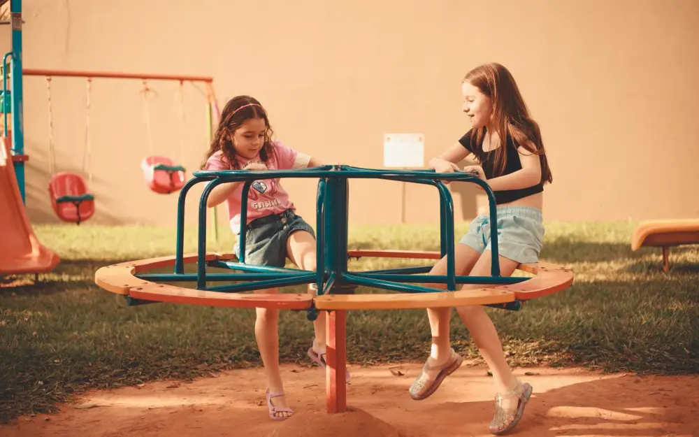 Symbolbild: Two girls enjoying a fun ride on a playground carousel under daylight.