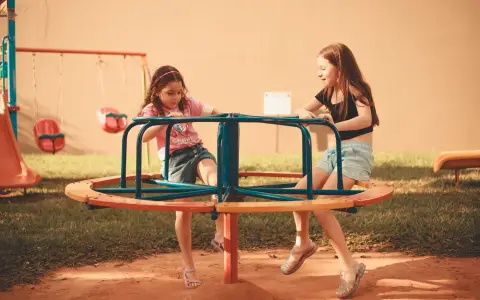 Symbolbild: Two girls enjoying a fun ride on a playground carousel under daylight.