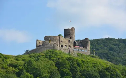 Symbolbild: A stunning view of a medieval hilltop castle surrounded by dense forest and clear skies.