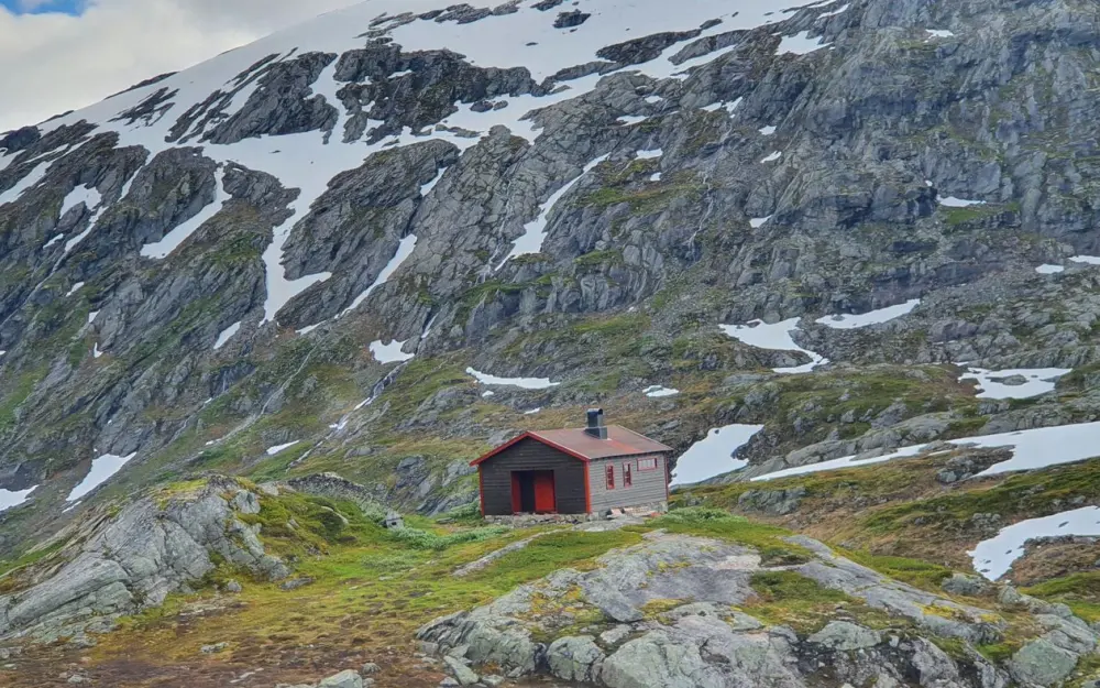 Symbolbild: A solitary cabin nestled in a rugged, snow-capped mountain, showcasing serene wilderness.