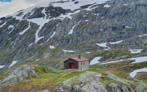 Symbolbild: A solitary cabin nestled in a rugged, snow-capped mountain, showcasing serene wilderness.