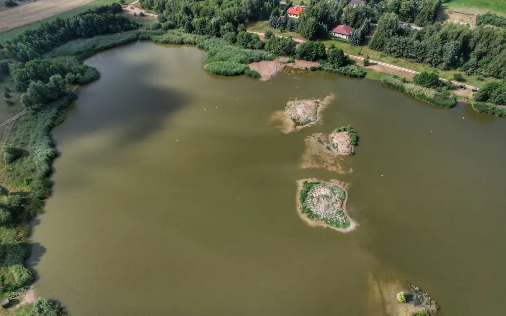 Symbolbild: Expansive aerial view of a tranquil lake surrounded by greenery and small islands.
