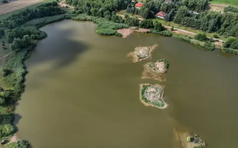 Symbolbild: Expansive aerial view of a tranquil lake surrounded by greenery and small islands.