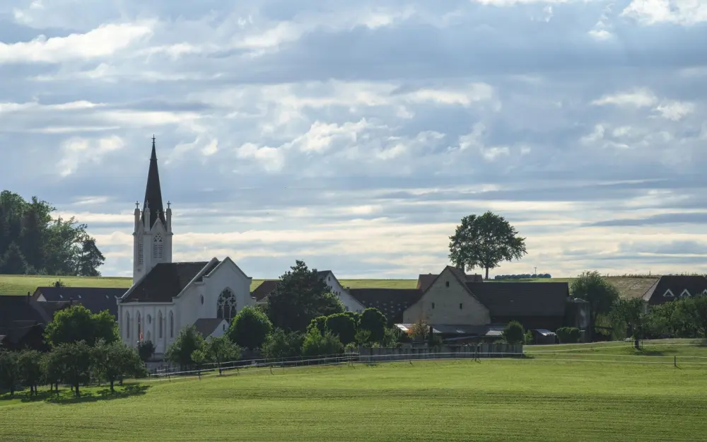 Symbolbild: Serene village scene with a church, lush meadow, and summer sky in Germany.