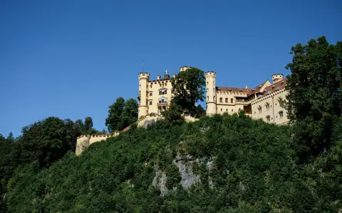 Symbolbild: Scenic view of Hohenschwangau Castle atop a hill in Füssen, perfect for travel and architecture enthusiasts.