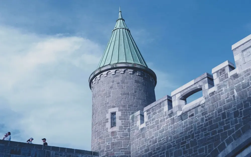 Symbolbild: Low angle view of a historic castle tower and walls under a blue sky.