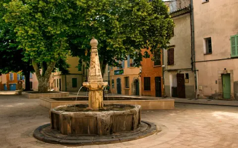 Symbolbild: Quaint European town square with a classic stone fountain and colorful buildings.