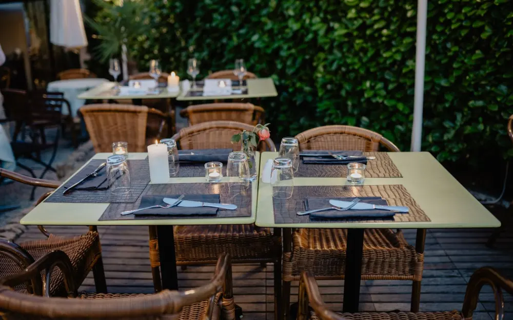 Symbolbild: Intimate outdoor dining setting with wicker chairs and candlelit tables on a charming terrace.