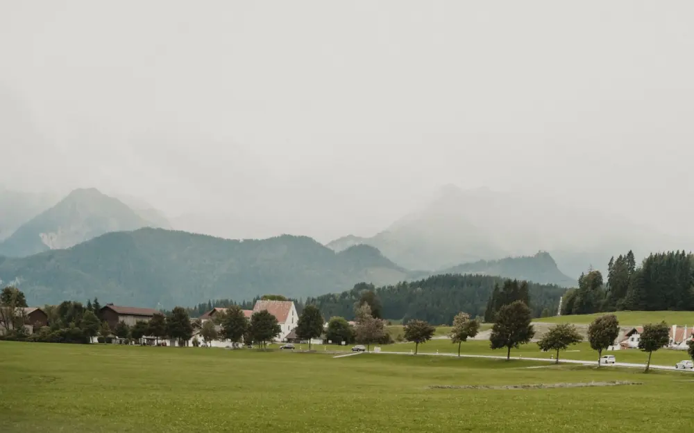 Symbolbild: Charming Bavarian village landscape with mountains in Baiern, Germany, under a cloudy sky.