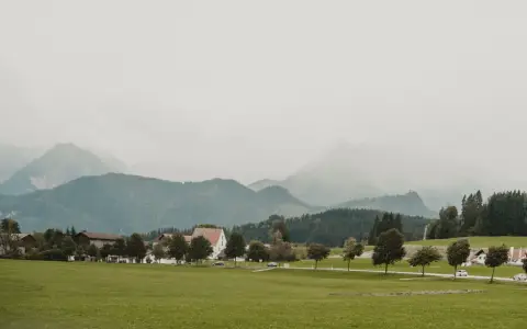 Symbolbild: Charming Bavarian village landscape with mountains in Baiern, Germany, under a cloudy sky.