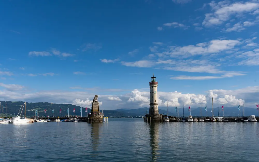 Beautiful view of Lindau Harbor with iconic lighthouse and statue, surrounded by calm lake waters.