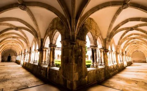Symbolbild: Explore the stunning Gothic architecture of Batalha Monastery's cloisters in Portugal with intricate vaulted ceilings.