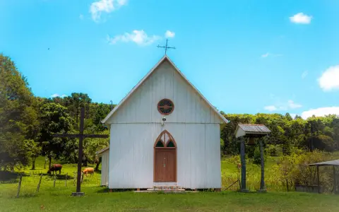 Symbolbild: Charming rural church amidst lush greenery on a bright summer day.
