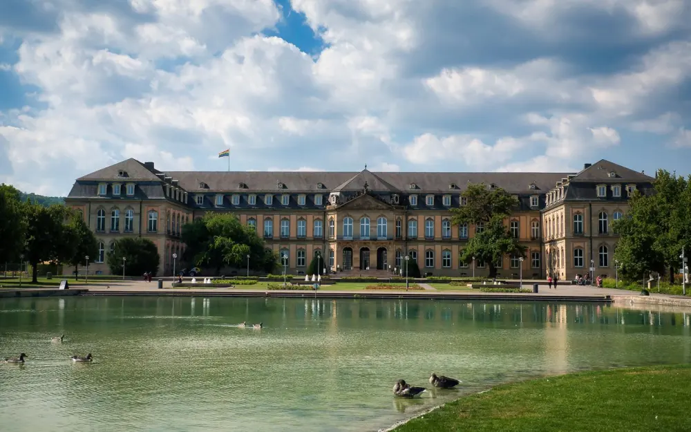 Symbolbild: The Neue Schloss in Stuttgart captured on a sunny day with serene ducks by the pond, showcasing urban elegance.
