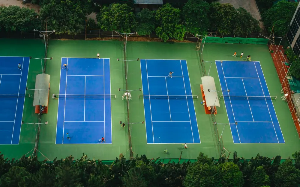 Symbolbild: Tennis courts from above showcasing players in action, surrounded by greenery.