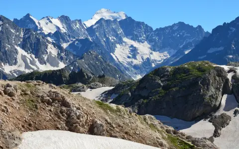 Symbolbild: Breathtaking view of a rocky mountain range with snow-capped peaks under a clear blue sky.