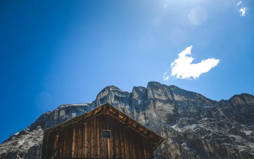 Symbolbild: Wooden cabin against a rugged mountain backdrop beneath a vibrant blue sky, ideal for travel inspiration.