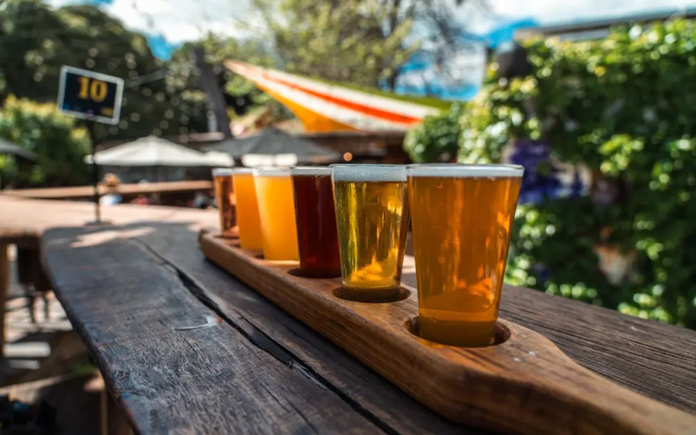 Symbolbild: A vibrant beer flight displayed on a rustic wood table outdoors during a sunny day.