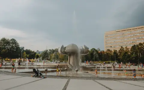 Symbolbild: A lively urban park with a modern fountain where families and children enjoy playing in the water.