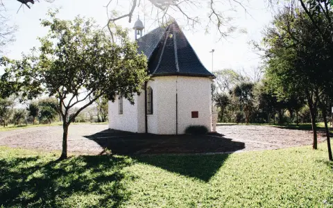Symbolbild: Quaint chapel nestled in a serene park setting bathed in sunlight.