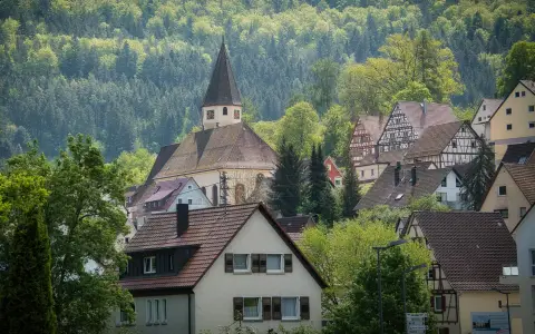 Symbolbild: Quaint German village scene with traditional houses and church amid vibrant green foliage.
