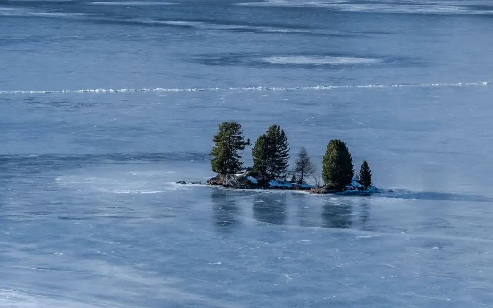 Symbolbild: A serene view of a frozen lake with a small tree-covered island in Grisons, Switzerland.