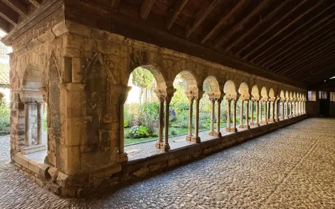Symbolbild: Medieval cloisters with stone arches in a tranquil garden setting in southern France.