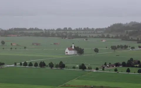 Symbolbild: Aerial view of a picturesque Bavarian village with a central chapel surrounded by lush green fields.