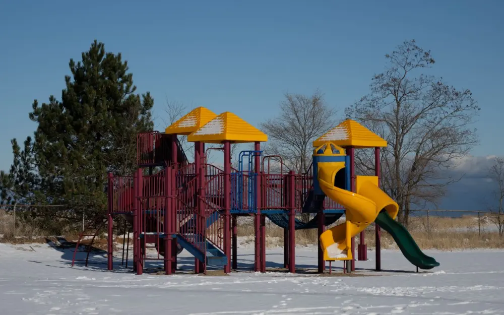 Symbolbild: Colorful playground equipment blanketed in snow on a clear winter day.