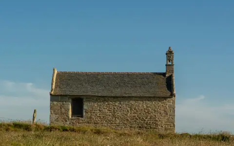 Symbolbild: A solitary stone chapel under a clear blue sky, surrounded by serene countryside.