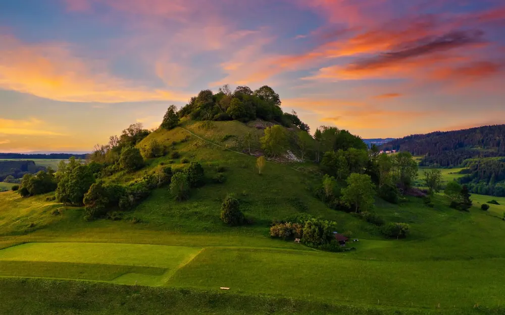 Symbolbild: A beautiful sunset over a lush green hilltop, capturing nature's serene beauty.