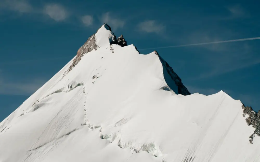 Symbolbild: Stunning snow-covered alpine mountain peak against a clear blue sky, showcasing natural beauty.