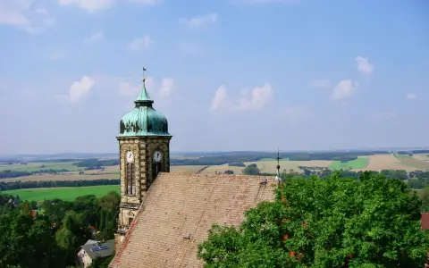 Symbolbild: Rustic German church tower amidst lush countryside beneath a vibrant blue sky.
